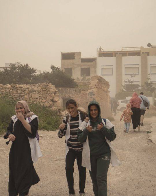 Three girls laughing in a dusty street
